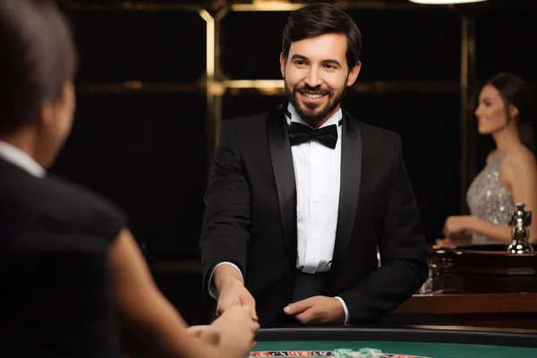 Nainen ylellisessä vihreässä iltapuvussa koristeellisen rulettipyörän vieressä, vangiten SPINARA:n tasokkaan kasinotunnelman.